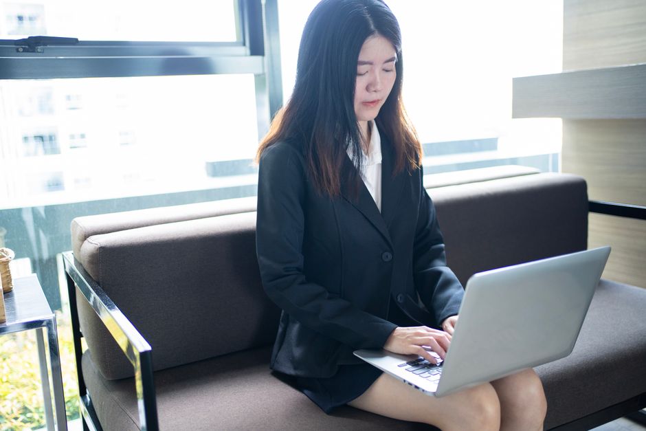 Asian woman in modern office setting, working remotely on a laptop.