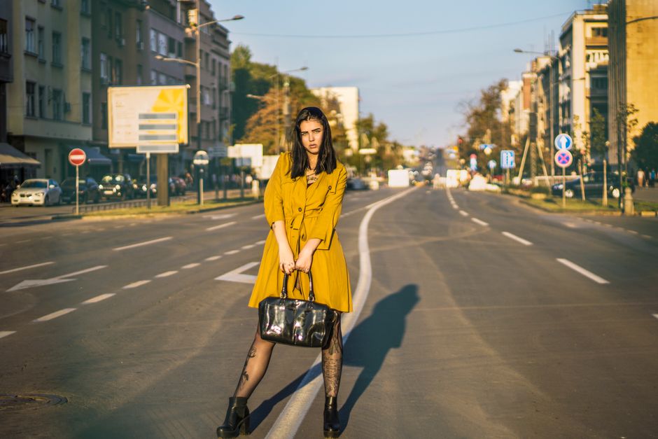 Fashionable woman in a mustard coat posing on an empty city street.