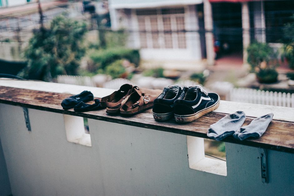 Sandals, sneakers, and socks arranged on a ledge, drying in the outdoor environment.