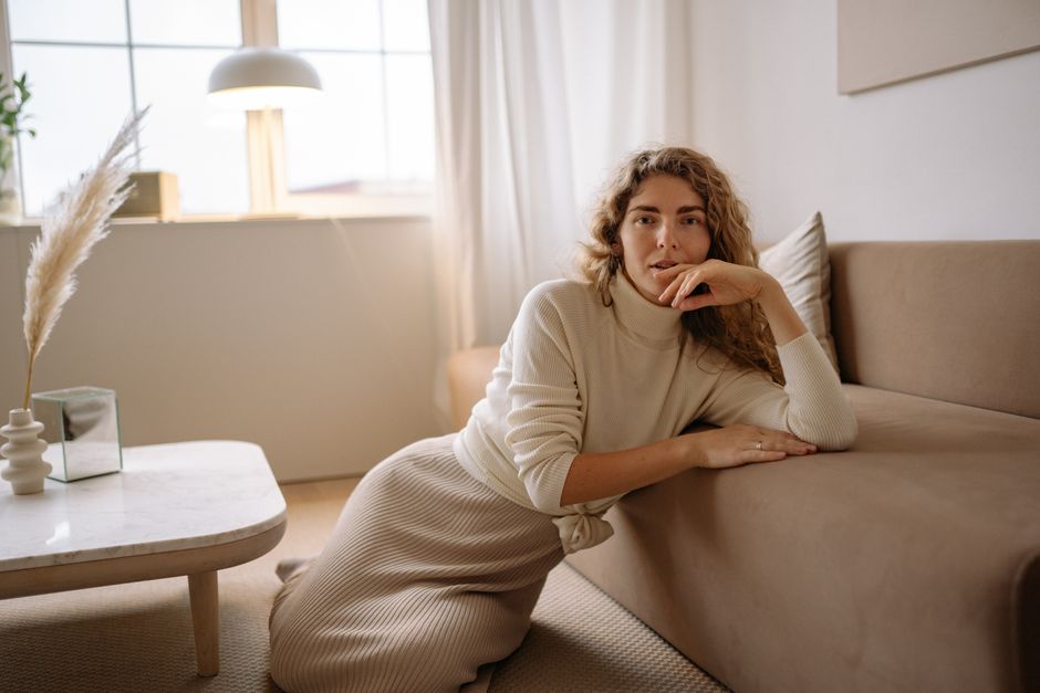 A woman leans on a sofa in a chic, cozy minimalist interior space.