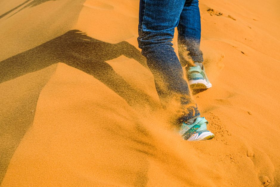Close-up of legs walking through golden desert sand, showcasing adventure and exploration.