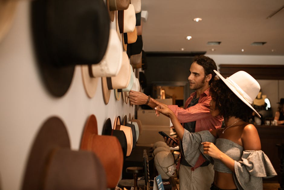 A man and woman checking a variety of hats displayed on a store wall.