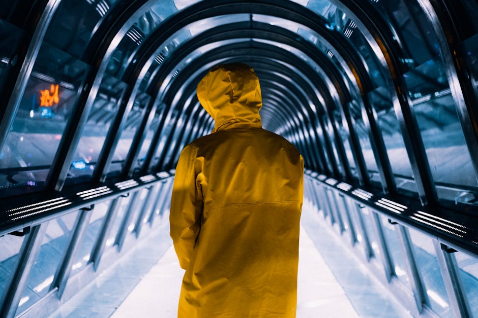 A person in a yellow jacket walks through a futuristic illuminated tunnel, showcasing urban symmetry.