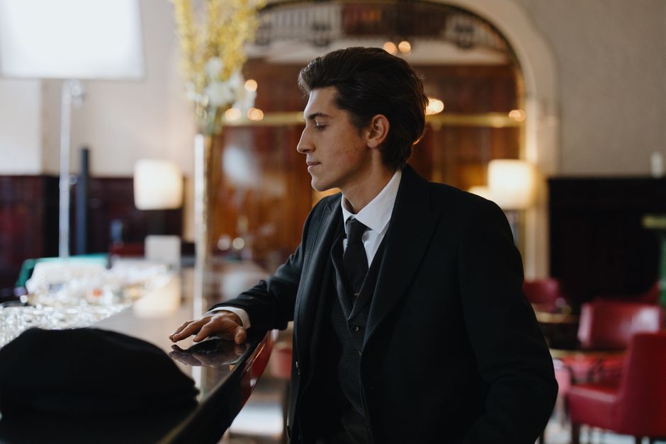 Stylish gentleman in formal attire sitting at a sophisticated bar counter indoors.
