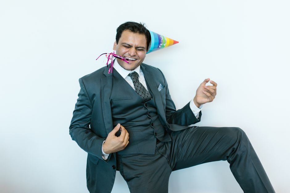 Joyful man in a suit celebrating with a colorful party hat and noisemaker.
