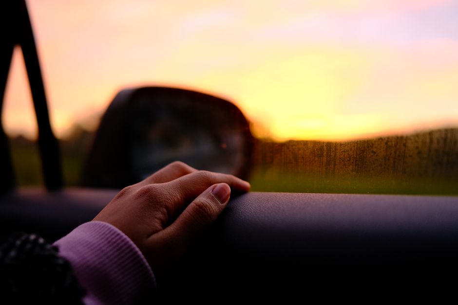 Close-up of a hand on a car window during a vibrant sunset in Brakel, Belgium.