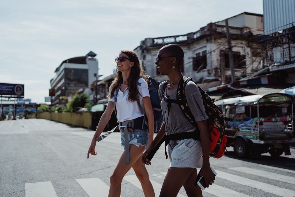Two women walking on a city street with backpacks, highlighting urban travel.