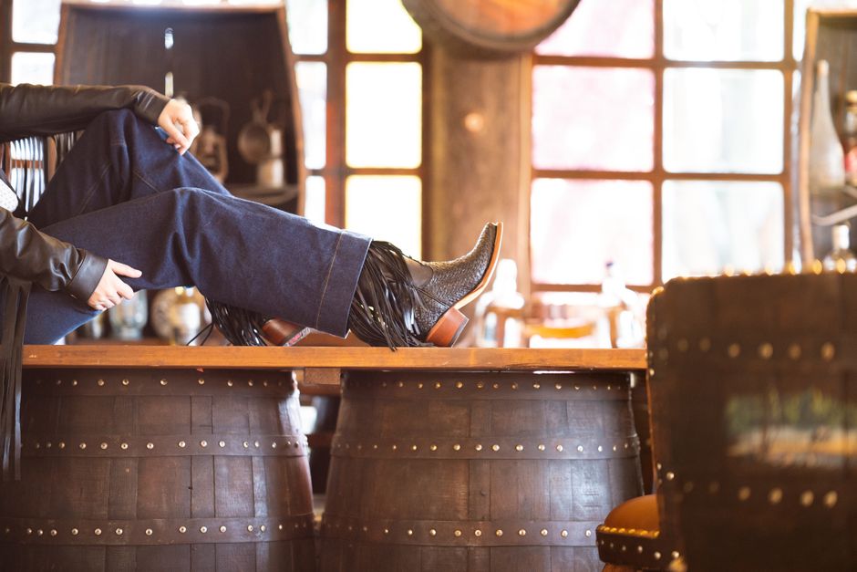 Cowboy boots resting on a whiskey barrel table in a rustic indoor setting, showcasing West