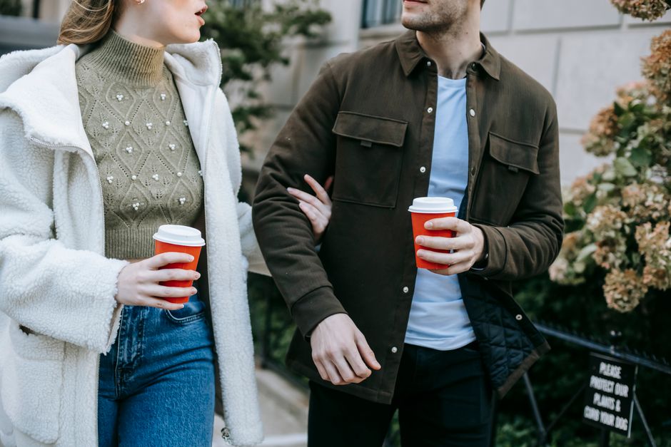 Crop anonymous young couple in stylish clothes drinking takeaway coffee and talking while
