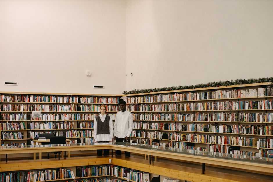 Two students standing in a modern library with extensive bookshelves.