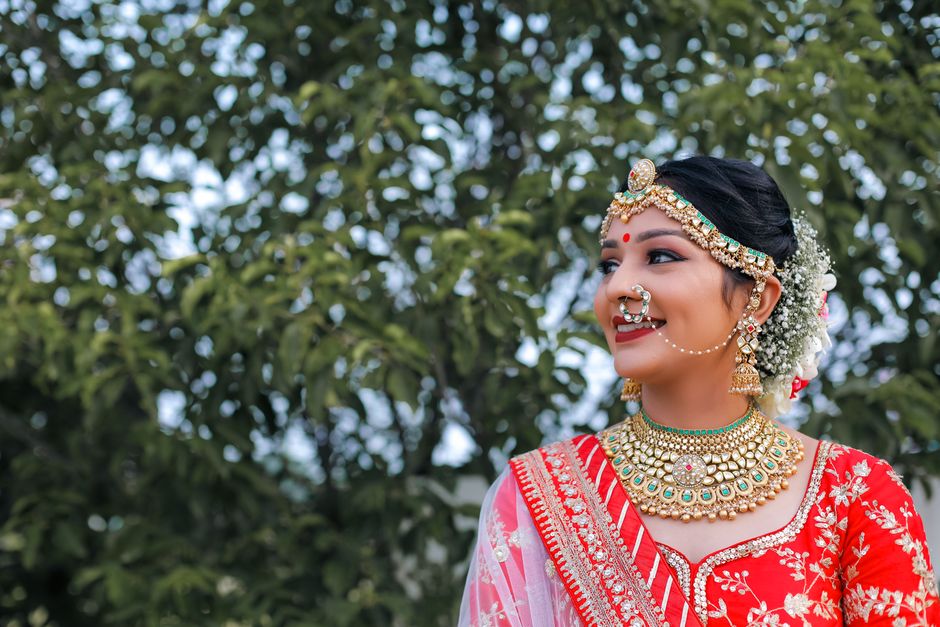 Beautiful Indian bride in red lehenga smiling outdoors, showcasing traditional jewelry and attire.