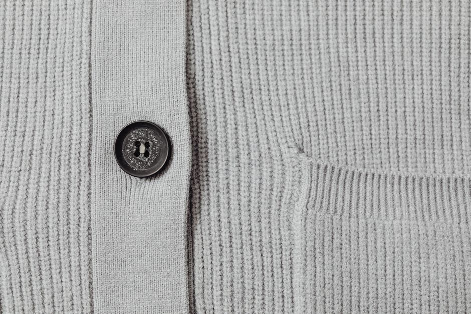 Detailed view of a gray knit cardigan featuring a black button and ribbed texture.