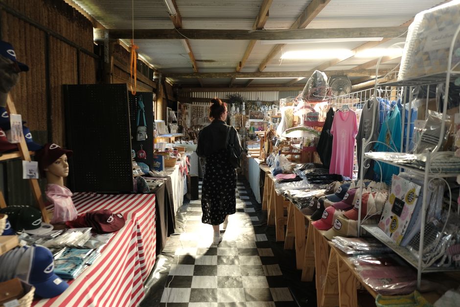 A woman browsing diverse products in an indoor market stall filled with hats and clothes.