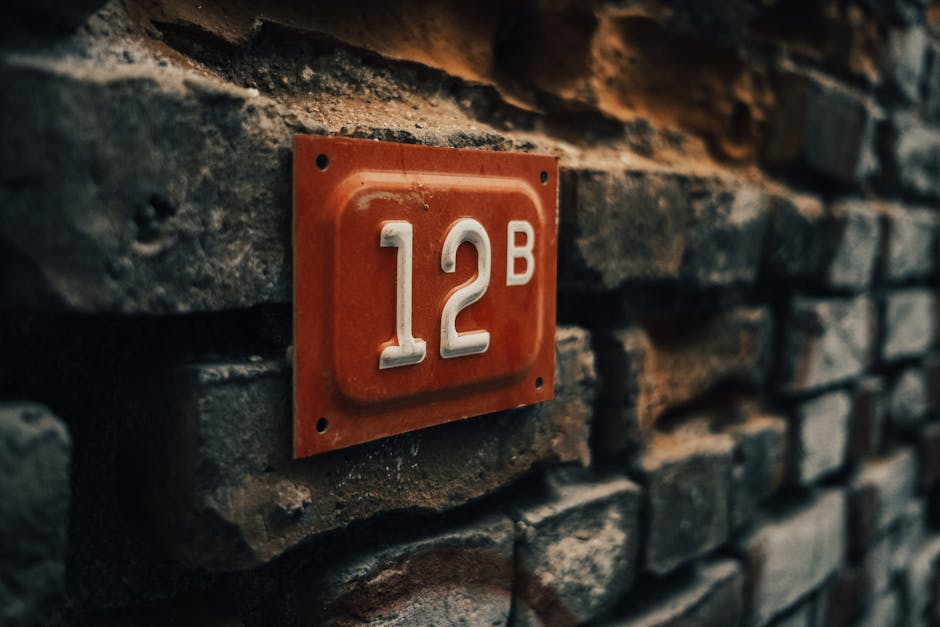 Close-up of a vintage apartment number 12B on a textured stone wall.