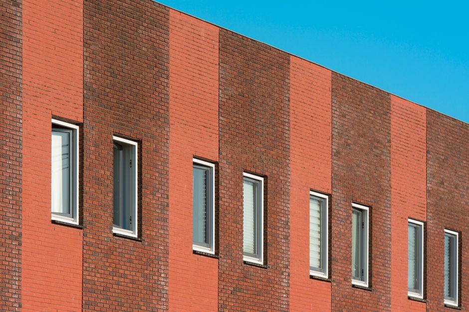 Close-up of a modern building's red brick wall and geometric window design against a blue sky.