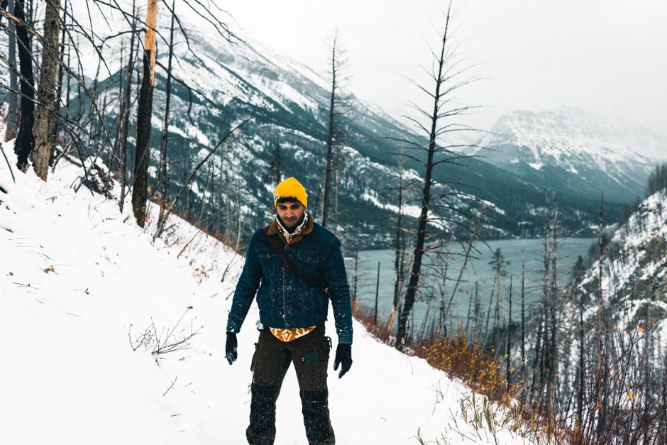 Man hiking in snowy Waterton Park, Alberta with scenic mountain and lake views.