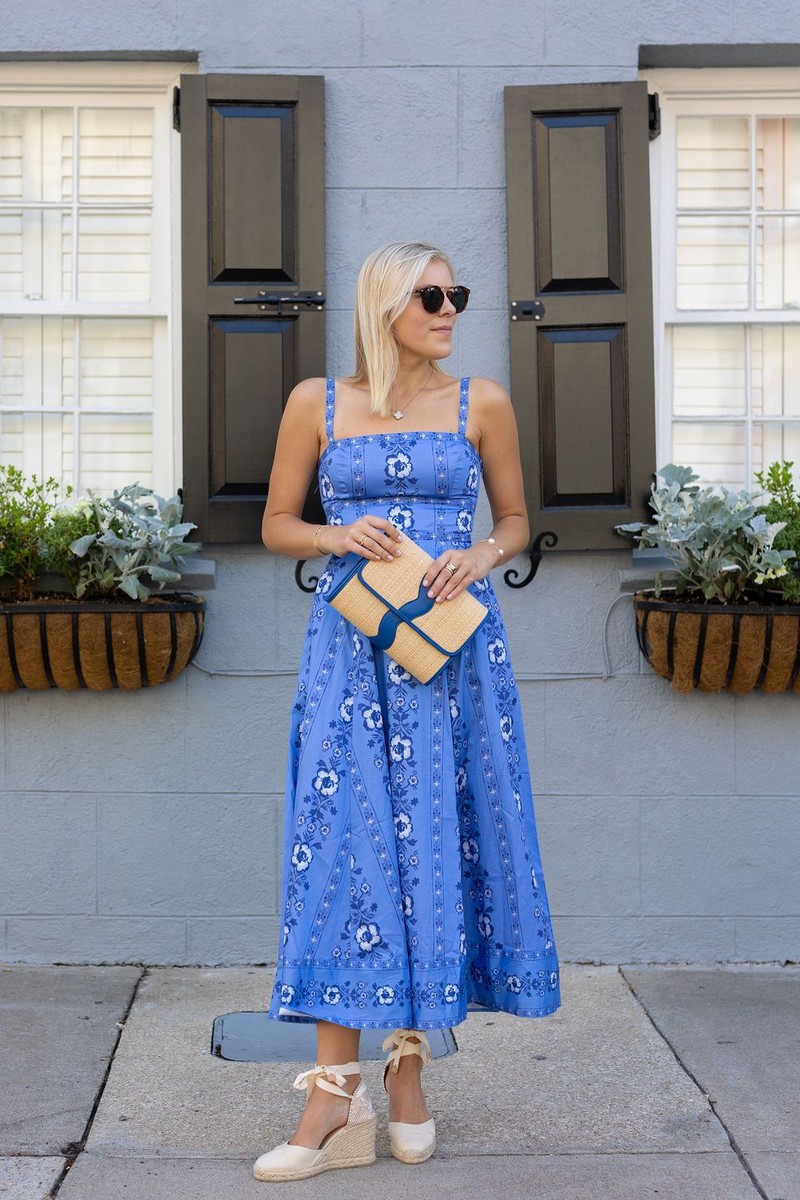 Woman in a blue dress holding a woven Allie rattan clutch