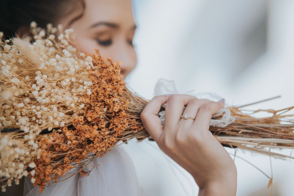 A close-up of a woman holding a bouquet of dried flowers, showcasing her elegant jewelry.