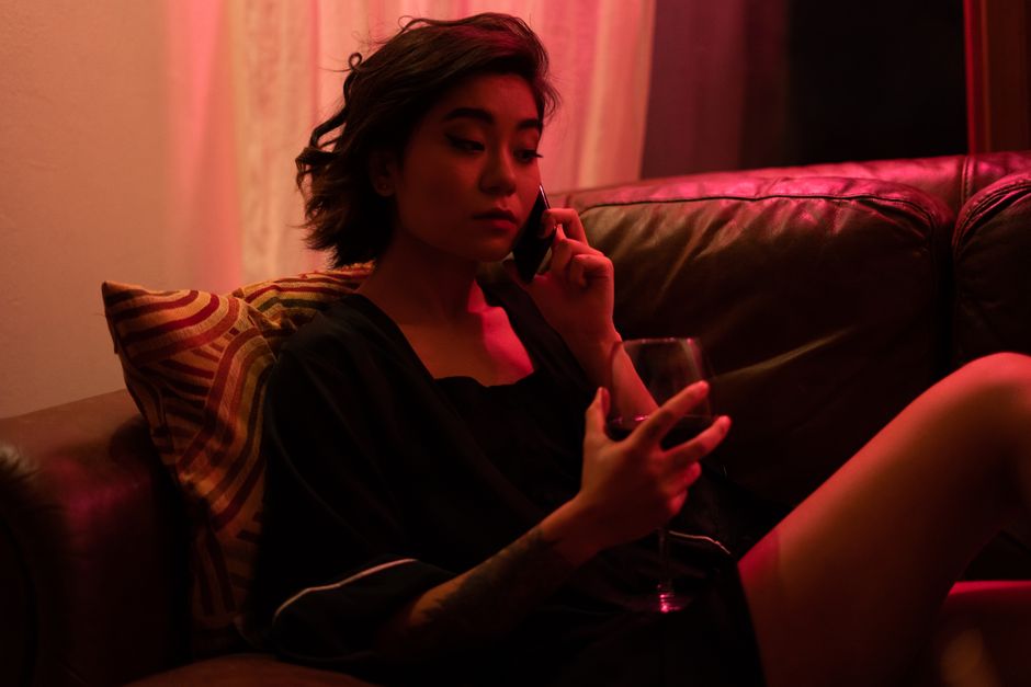 A woman relaxes on a sofa with a glass of wine, illuminated by atmospheric neon lighting.