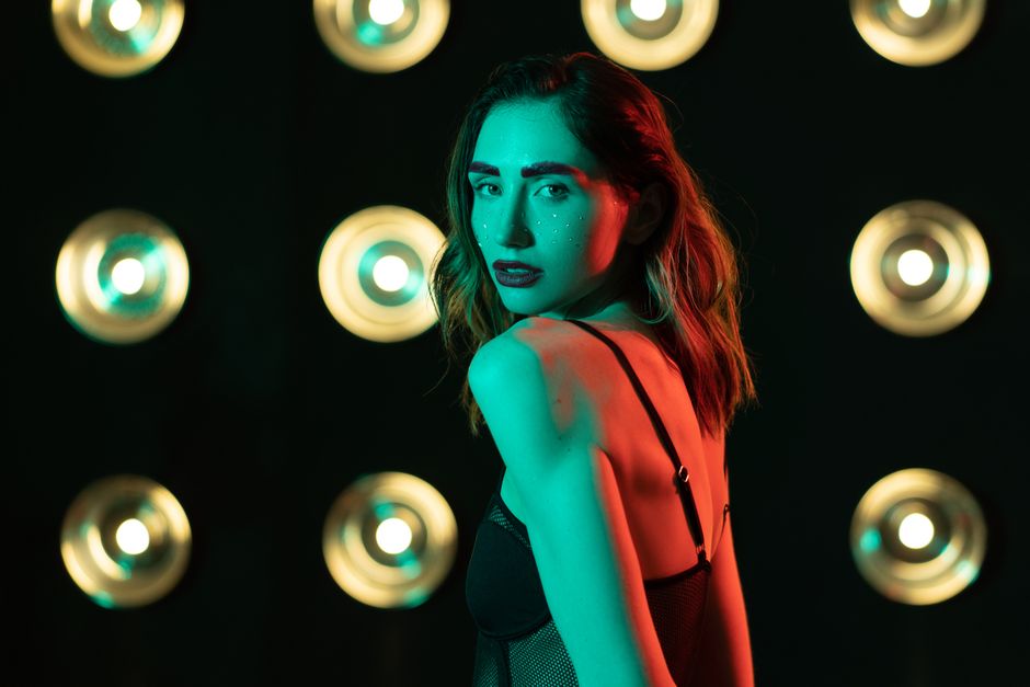 Fashionable woman posing with glitter makeup in colorful studio lighting.
