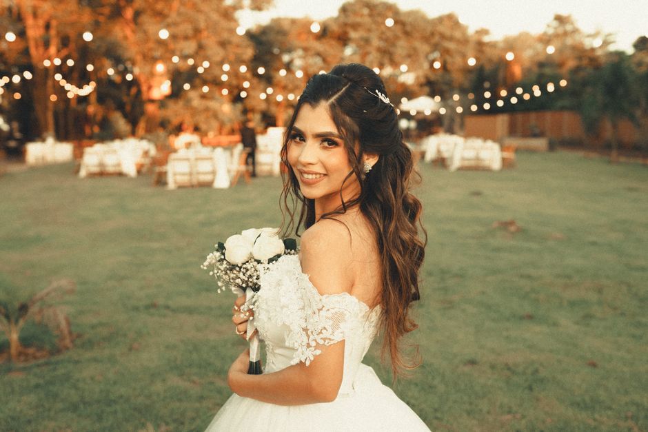 Beautiful bride smiling while holding bouquet in a stunning outdoor wedding setting.