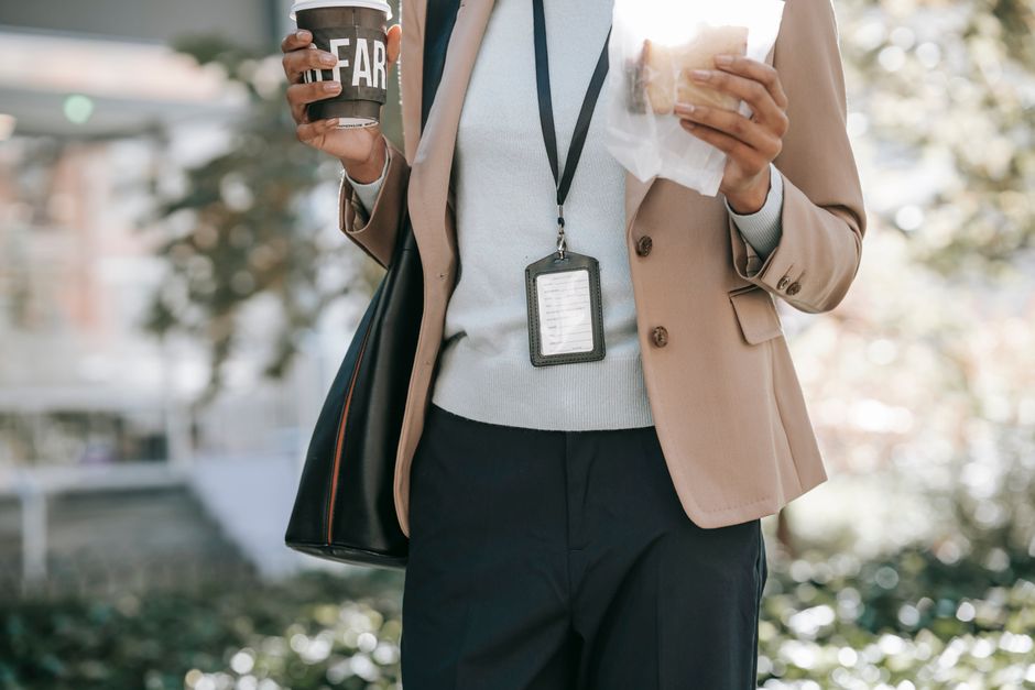 Crop anonymous ethnic female entrepreneur with takeaway hot drink and bread walking to work