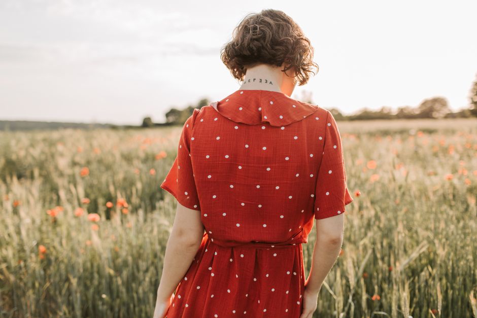 Back view of a woman in a red polka dot dress standing in a field with wildflowers at sunset.
