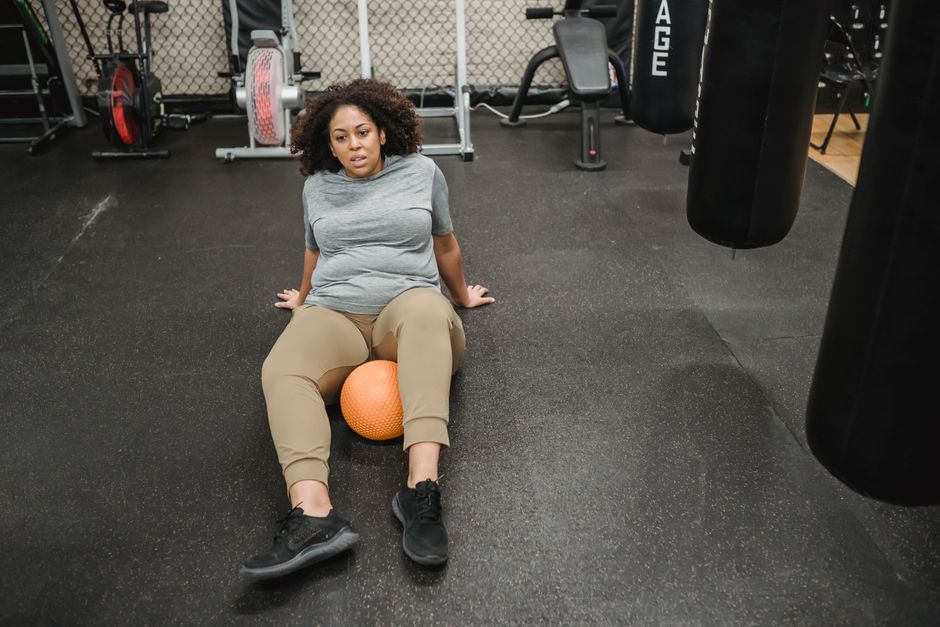 From above of plump African American overweight female exercising with ball on floor in sport club