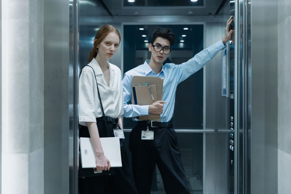 Two professionals in an elevator, standing with documents, in a corporate environment.
