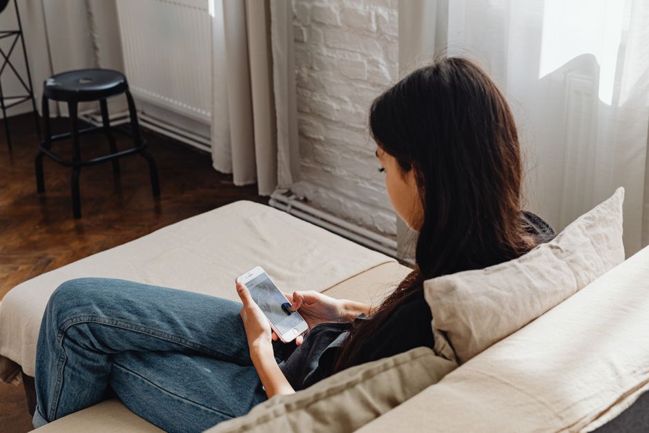 A woman sits comfortably on a sofa, browsing her smartphone in a cozy indoor setting.