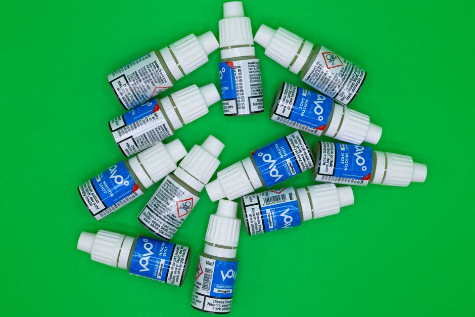 Top view of multiple nicotine vape shot bottles arranged on a green background.