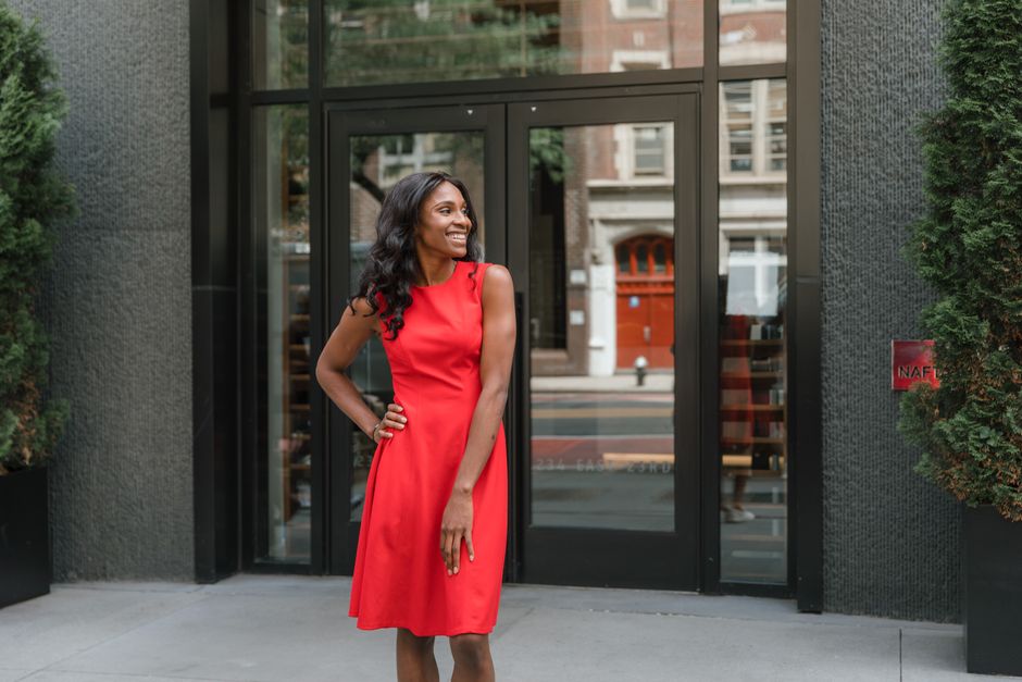 Stylish woman in a red dress stands confidently outdoors in front of a modern office building.