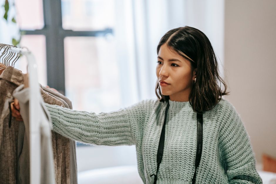 Young Latin American female looking away against collection of apparel on stand in house room