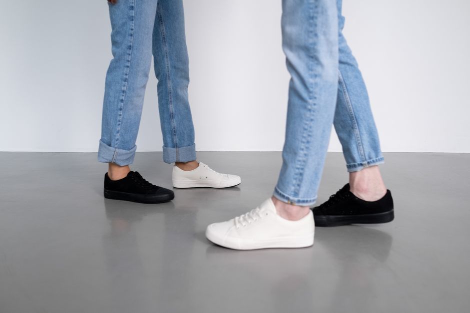 A fashion forward shot featuring black and white sneakers on a gray floor, with denim pants.