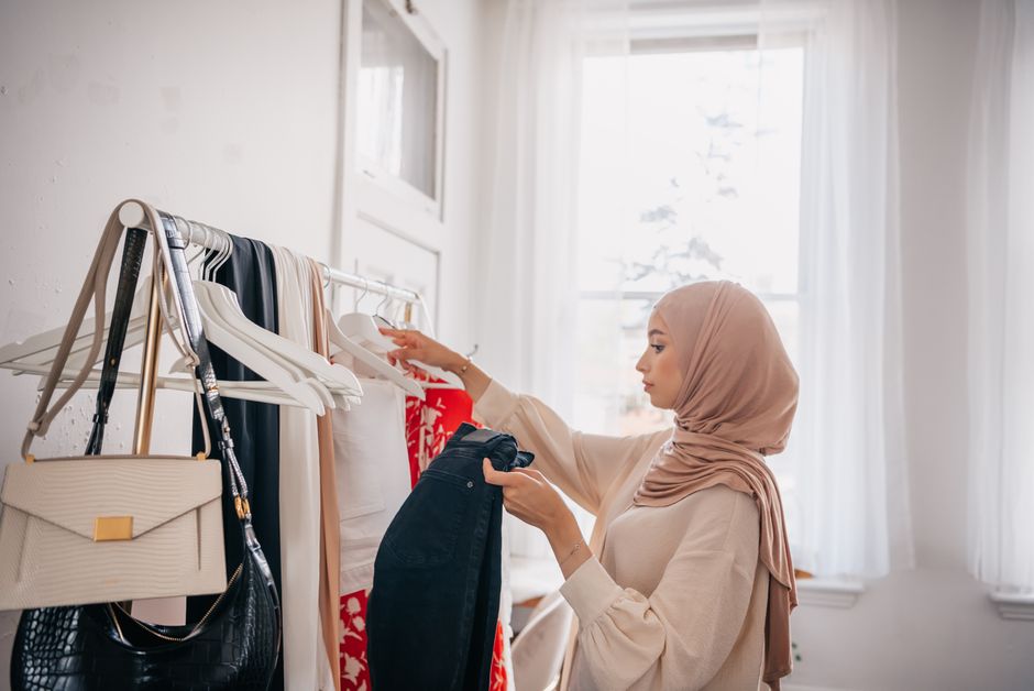 Young woman in hijab browsing clothes on rack indoors. Fashionable and modern.