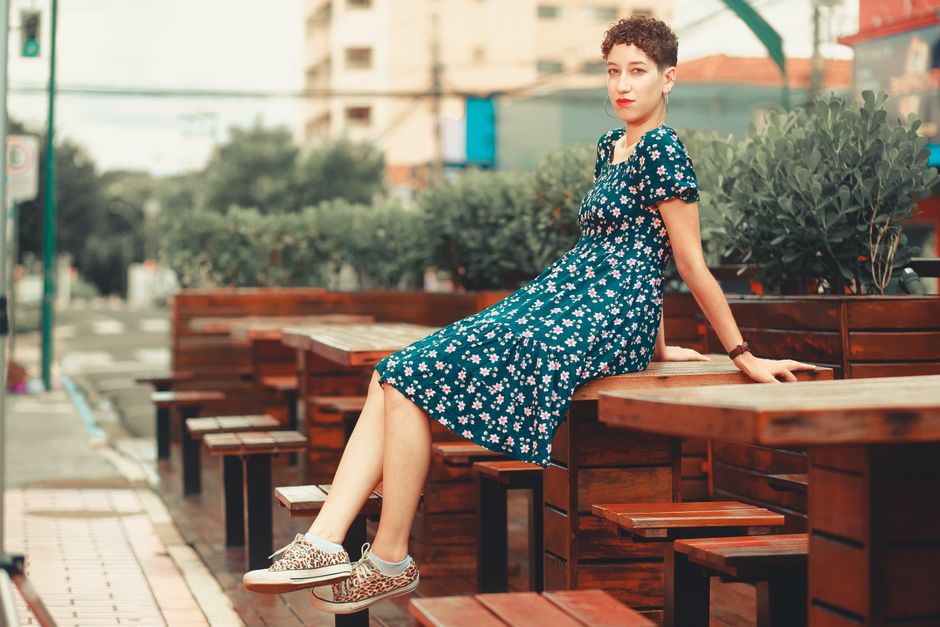 Fashionable woman in a floral sundress sitting at an urban outdoor cafe.