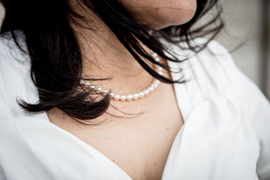 A close-up view of a woman wearing an elegant pearl necklace, complemented by her flowing dark hair and white blouse.