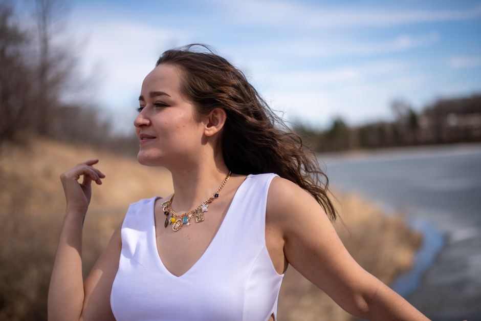 Young woman in a white dress with flowing hair by the lake on a windy day, embracing nature.