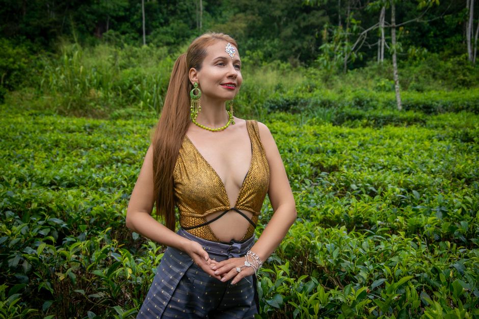 Stylish woman in glittering top with jewelry in lush green field.