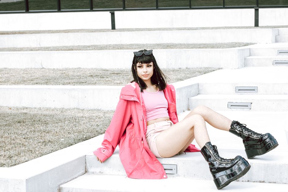 Stylish woman wearing pink jacket and platform boots sitting on outdoor stairs, exuding mo