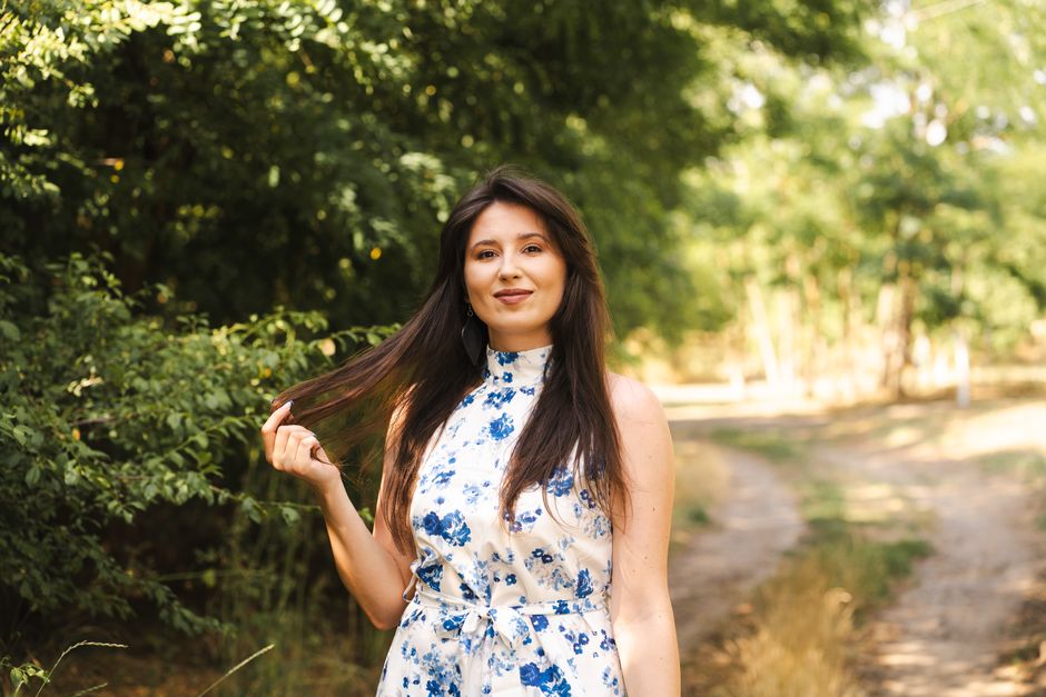 A woman in a blue floral dress enjoys a sunny day in nature, embodying summer bliss.