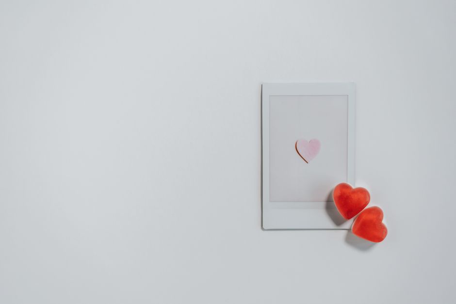 Top view of heart shaped red candy placed on white photo with heart image on white backgro