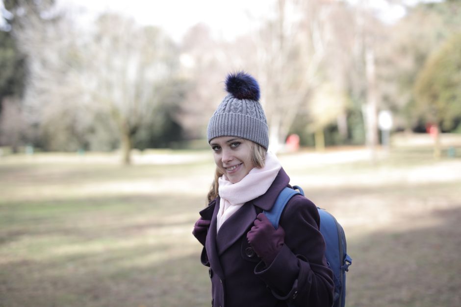 A happy woman with a backpack and beanie smiling in a scenic park setting.
