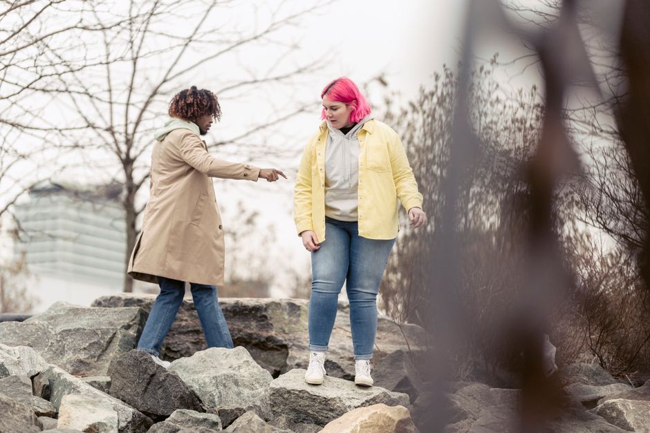 Two friends exploring a rocky outdoor setting, dressed casually. Urban background hints at city outskirts.