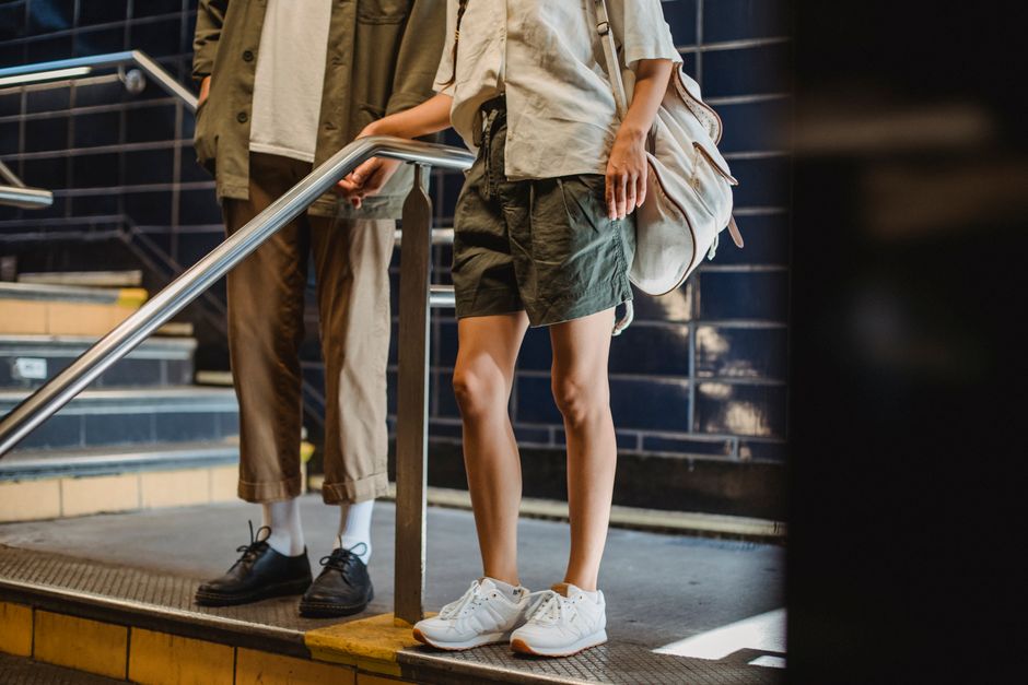 Crop anonymous couple in casual outfits standing near stairs railing in modern underground