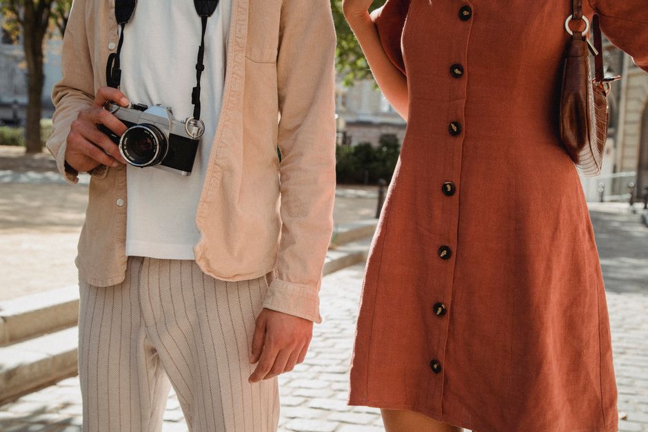 Stylish couple in casual chic attire strolling a sunny urban street with a vintage camera.