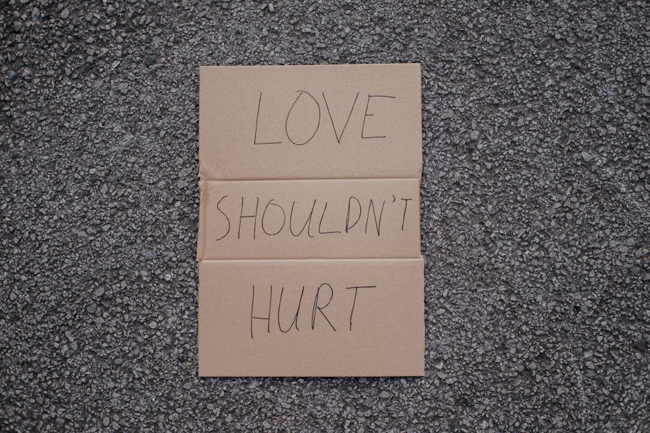 Cardboard sign on asphalt advocating against violence with the phrase 'Love Shouldn't Hurt.'