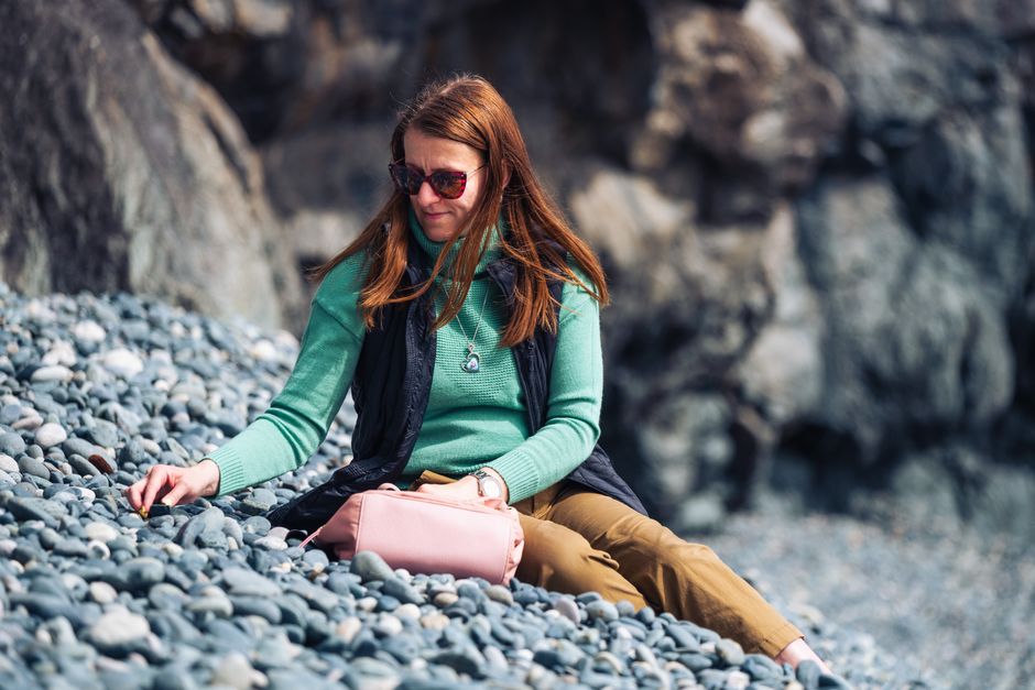 Woman enjoying solitude on a rocky beach at Jordan River, BC, collecting stones amidst scenic views.