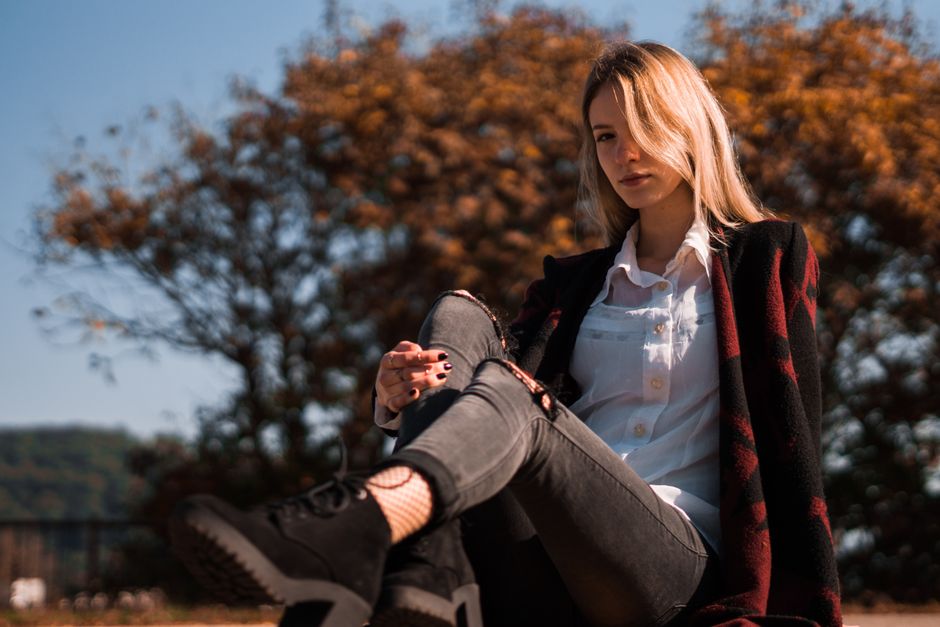 Young woman in fashionable attire sitting relaxed in a park during fall, capturing a seren
